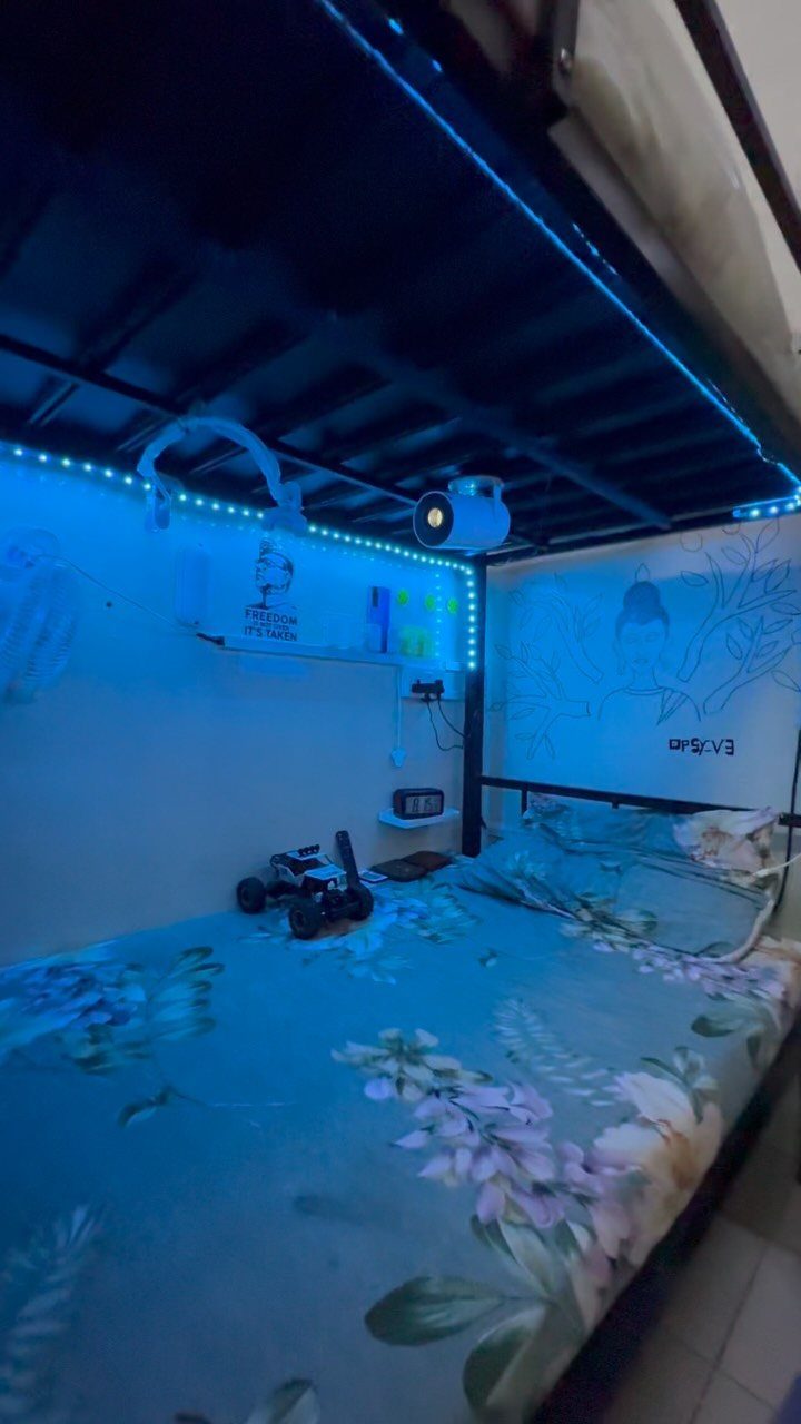 Bed with floral duvet under a bunk bed frame with blue LED lighting