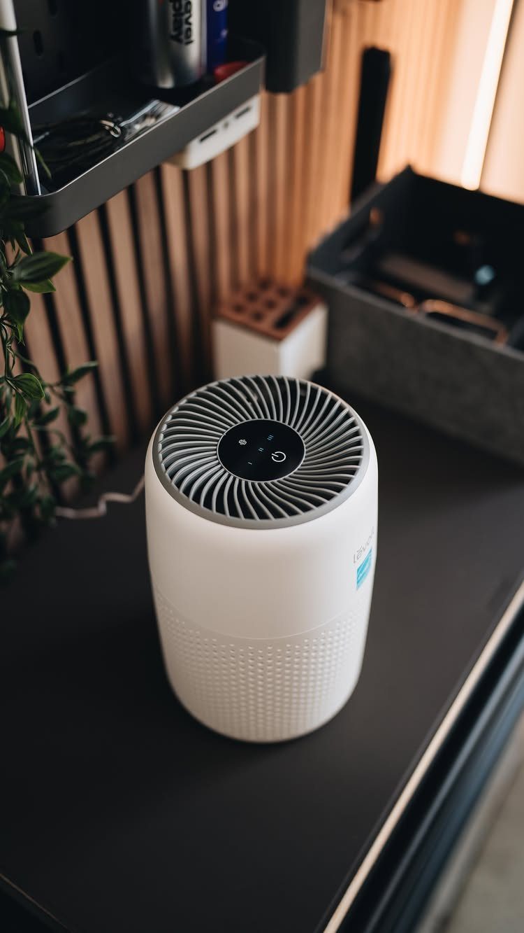 White cylindrical air purifier sitting on a dark grey desk in a room.