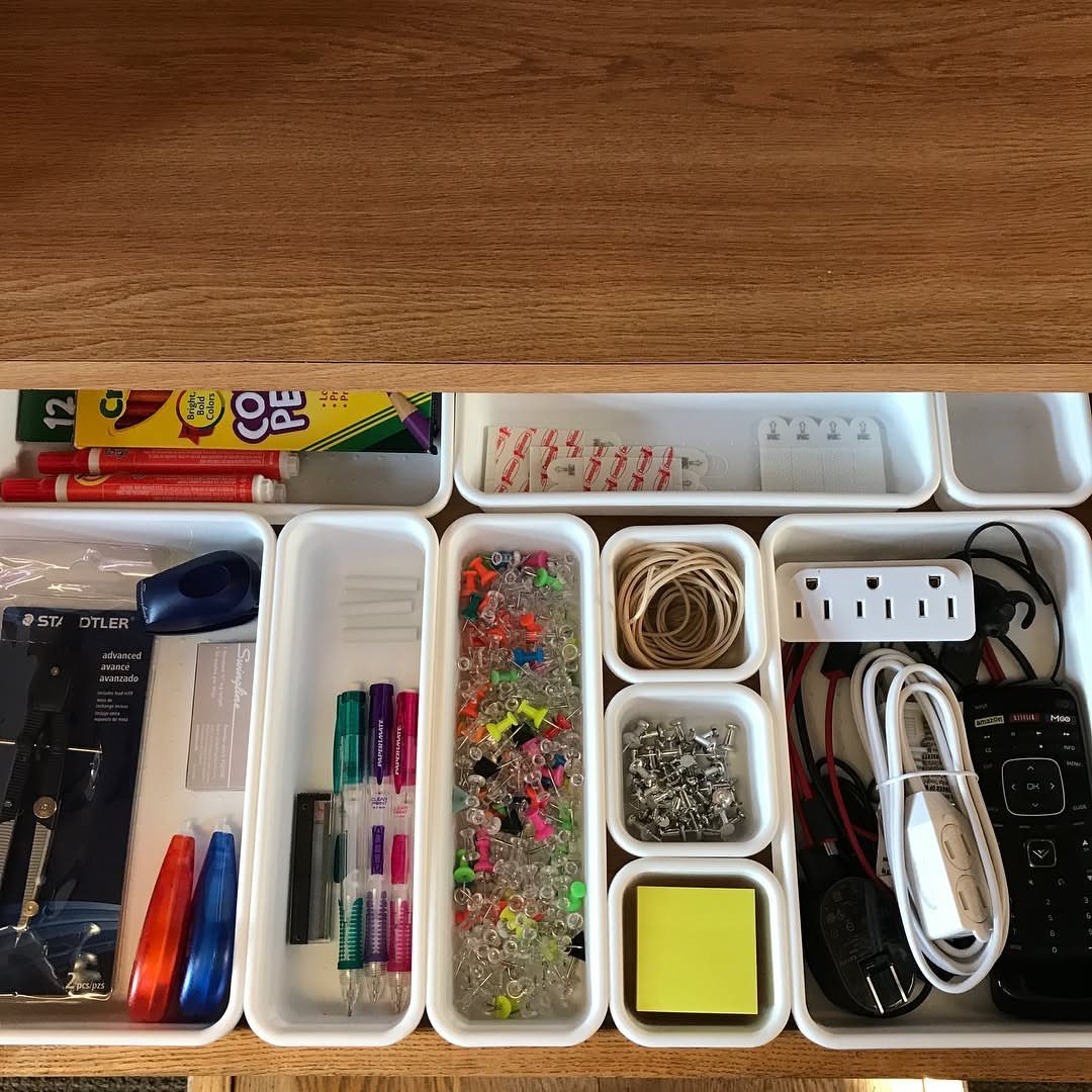 Organized wooden drawer with white bins holding stationery, beads, and electronic cables.