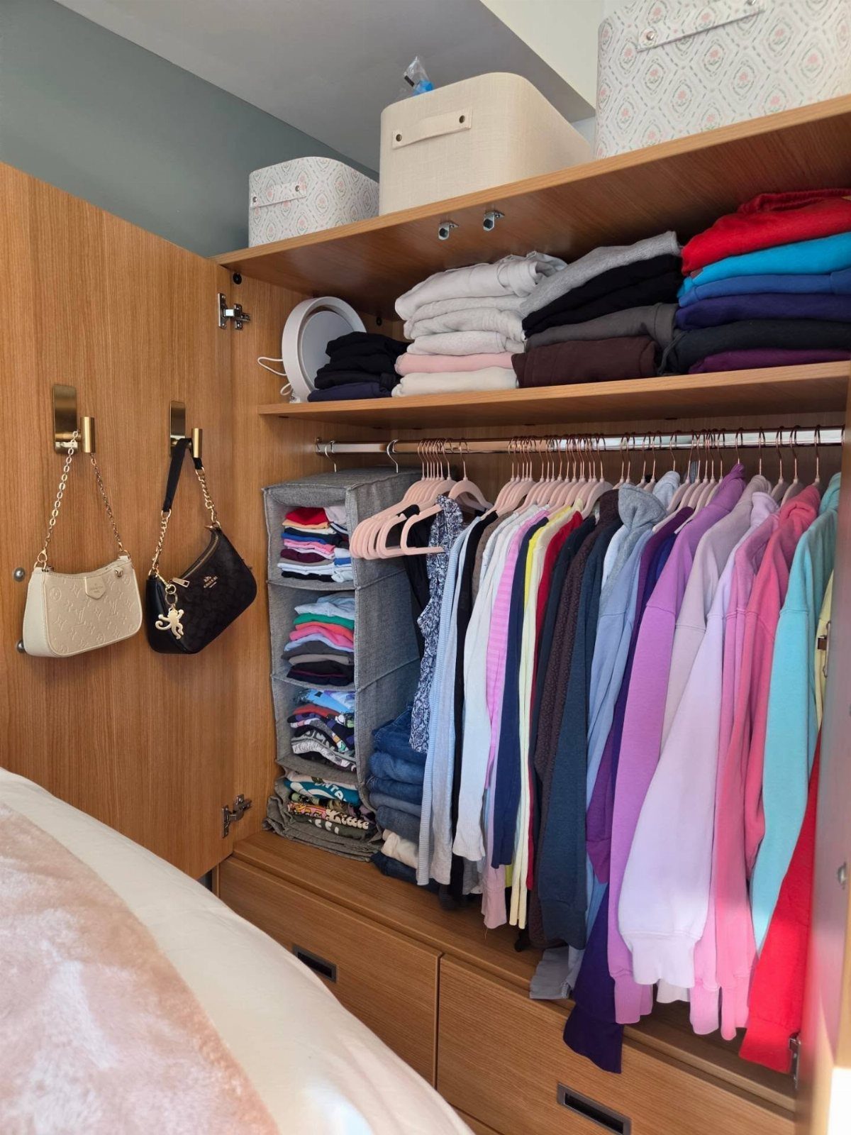 Organized wooden wardrobe with colorful hanging clothes, folded shirts, and hanging storage bins.