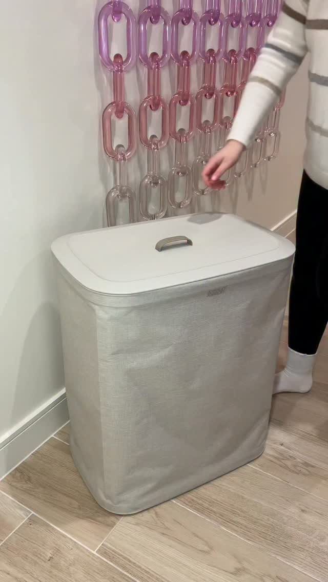 White fabric laundry hamper with lid standing on a light wood floor.