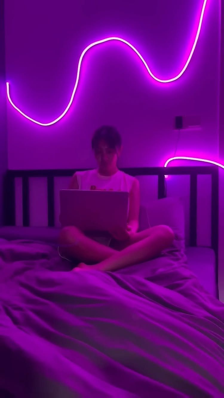 Person using a laptop on a bed under purple neon wave lights