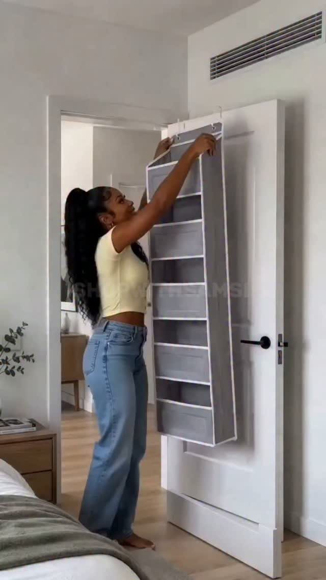 Woman hanging a grey fabric over-the-door organizer on a white bedroom door.