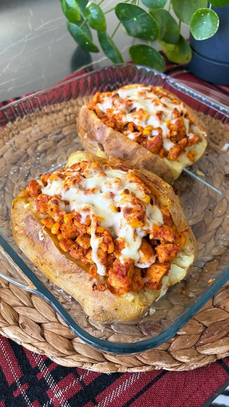 Two stuffed baked potatoes with seasoned meat and melted cheese in glass dish.