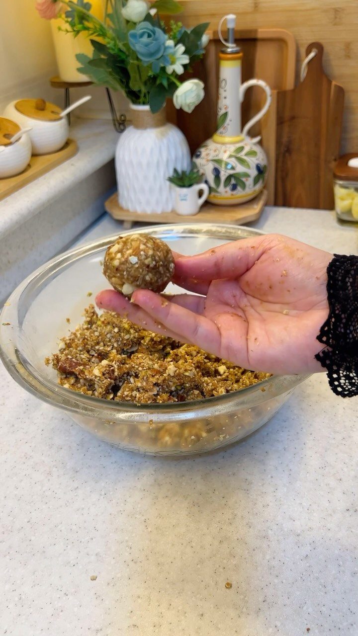 Hand holding a round energy bite over a bowl of oat mixture.
