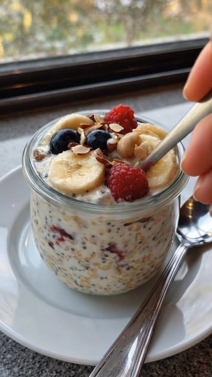 Overnight oats in a glass jar topped with fresh berries, bananas, and almonds.