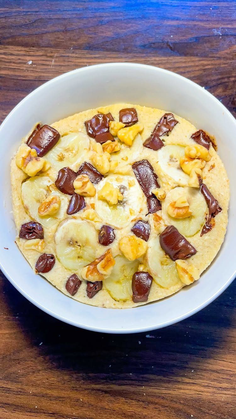 Rice cake topped with banana slices, walnuts, and chocolate in a white bowl.