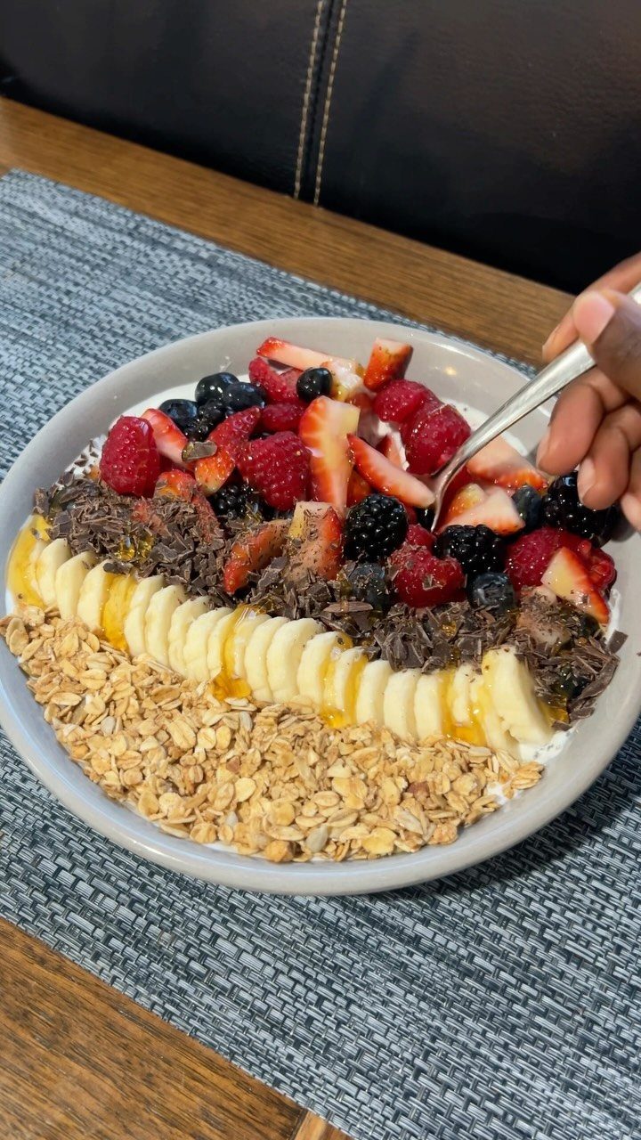 Yogurt parfait bowl topped with granola, bananas, chocolate, and fresh mixed berries.