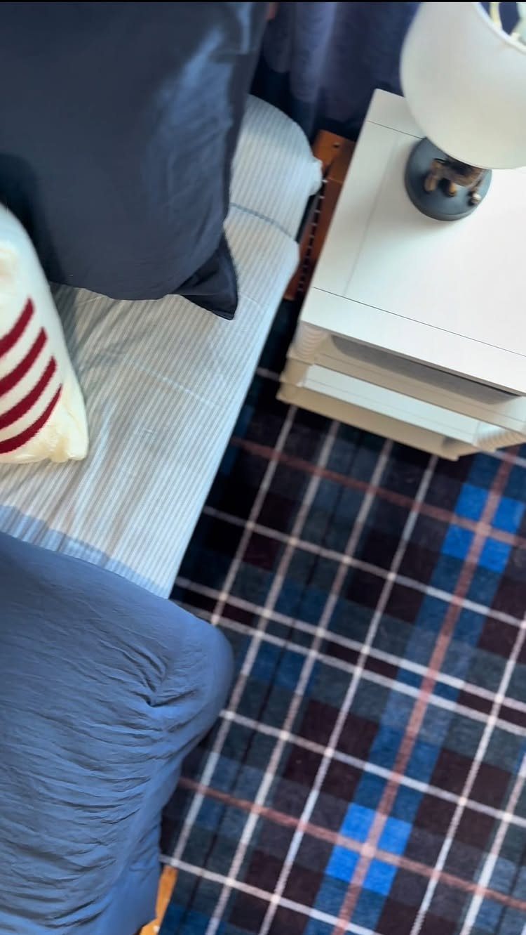 Blue and black plaid area rug next to a bed and white nightstand.