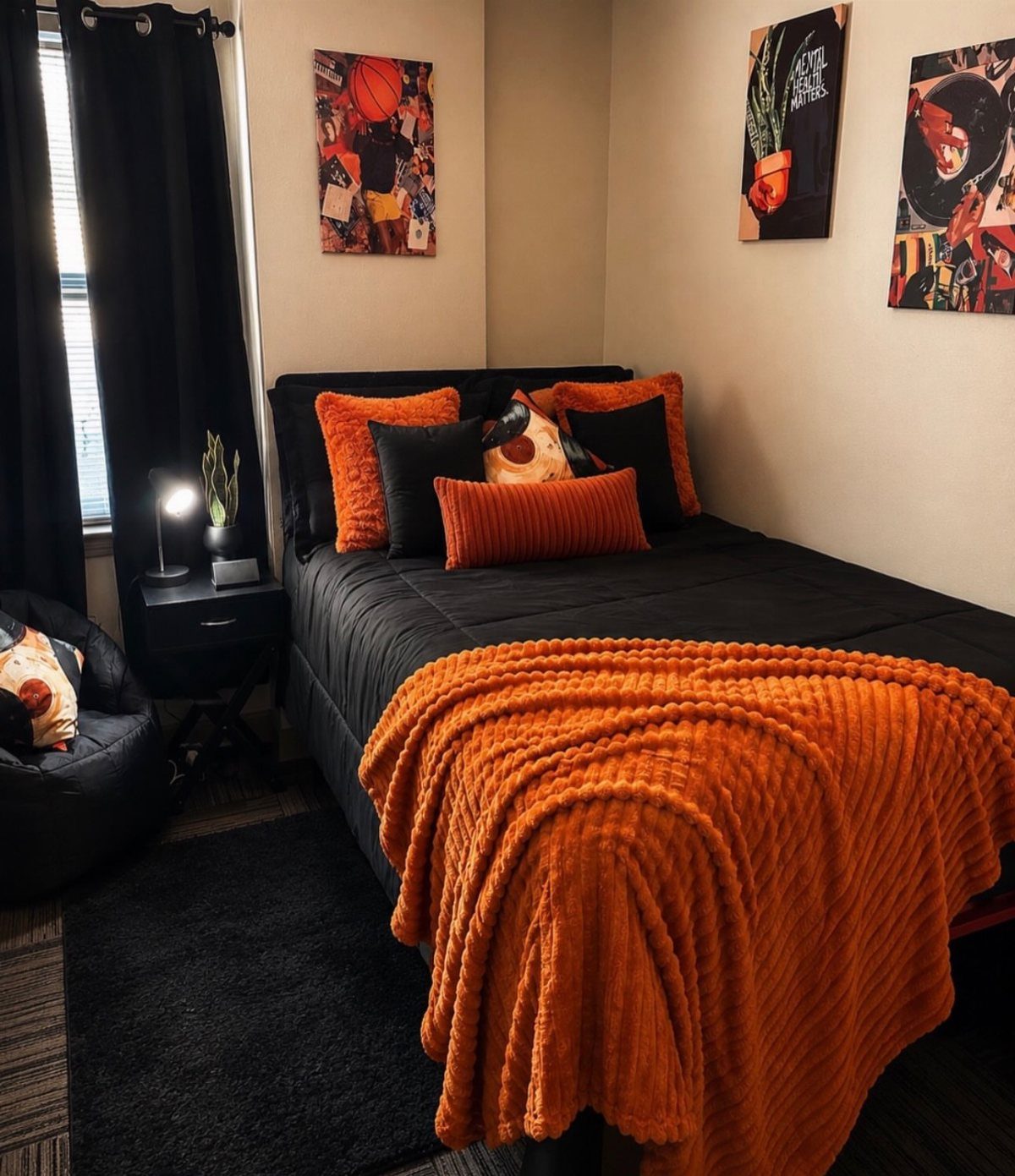 Bedroom with black and orange bedding, sports posters, and black furniture and curtains.