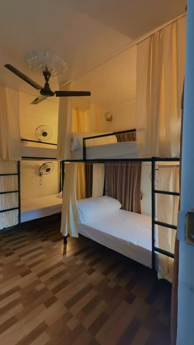 Bunk beds with white sheets and yellow curtains in a simple dorm room.