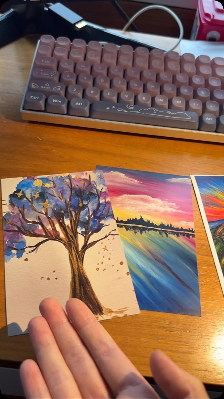 Hand-painted watercolor landscapes on a wooden desk next to a purple keyboard