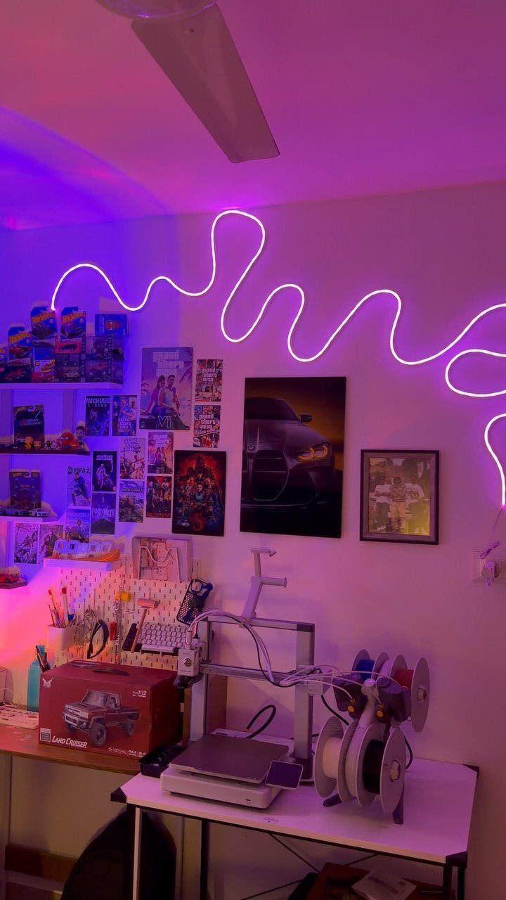 Wavy purple LED light strip on a wall above a desk and posters.