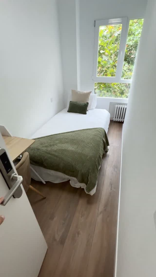 Small bedroom with a single bed, green blanket, and a simple wooden desk.