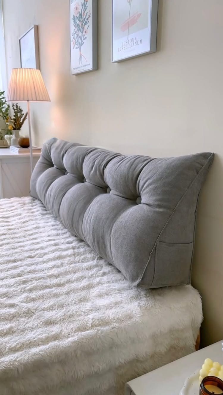 Grey tufted pillow headboard on a bed with white fluffy bedding and wall art.