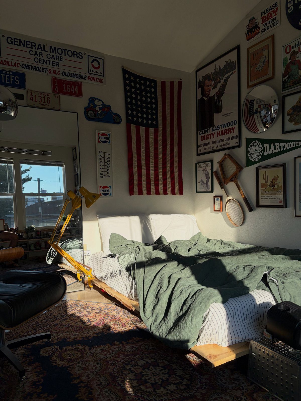 US flag and vintage posters hanging on a white wall above a bed.