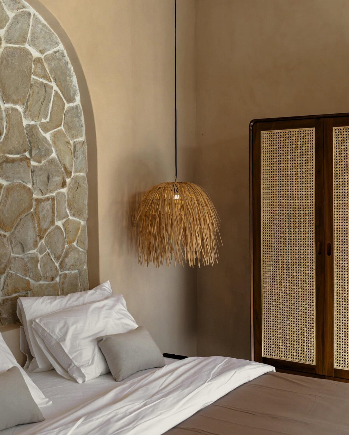 Bedroom with textured beige walls, an arched stone feature, and woven straw lighting.