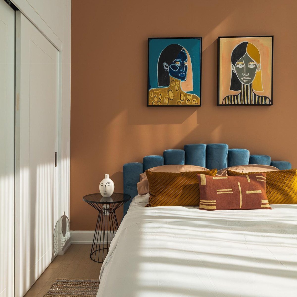 Rust-colored bedroom wall with a blue headboard and matching rust-toned decorative pillows.
