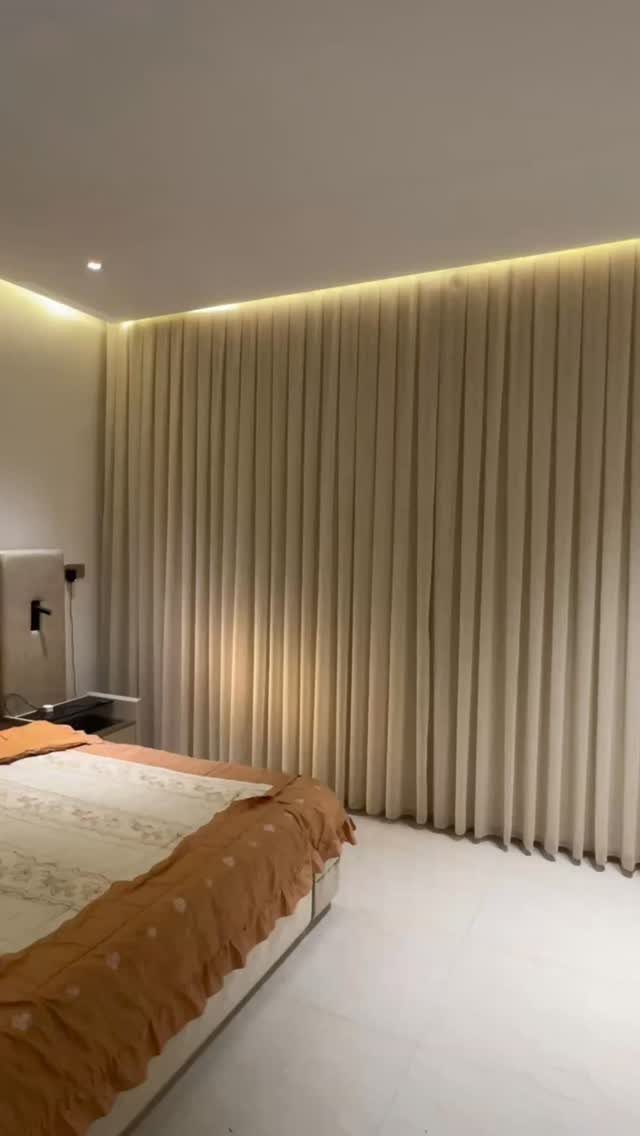 Beige pleated drapery covering a bedroom wall with warm overhead cove lighting.