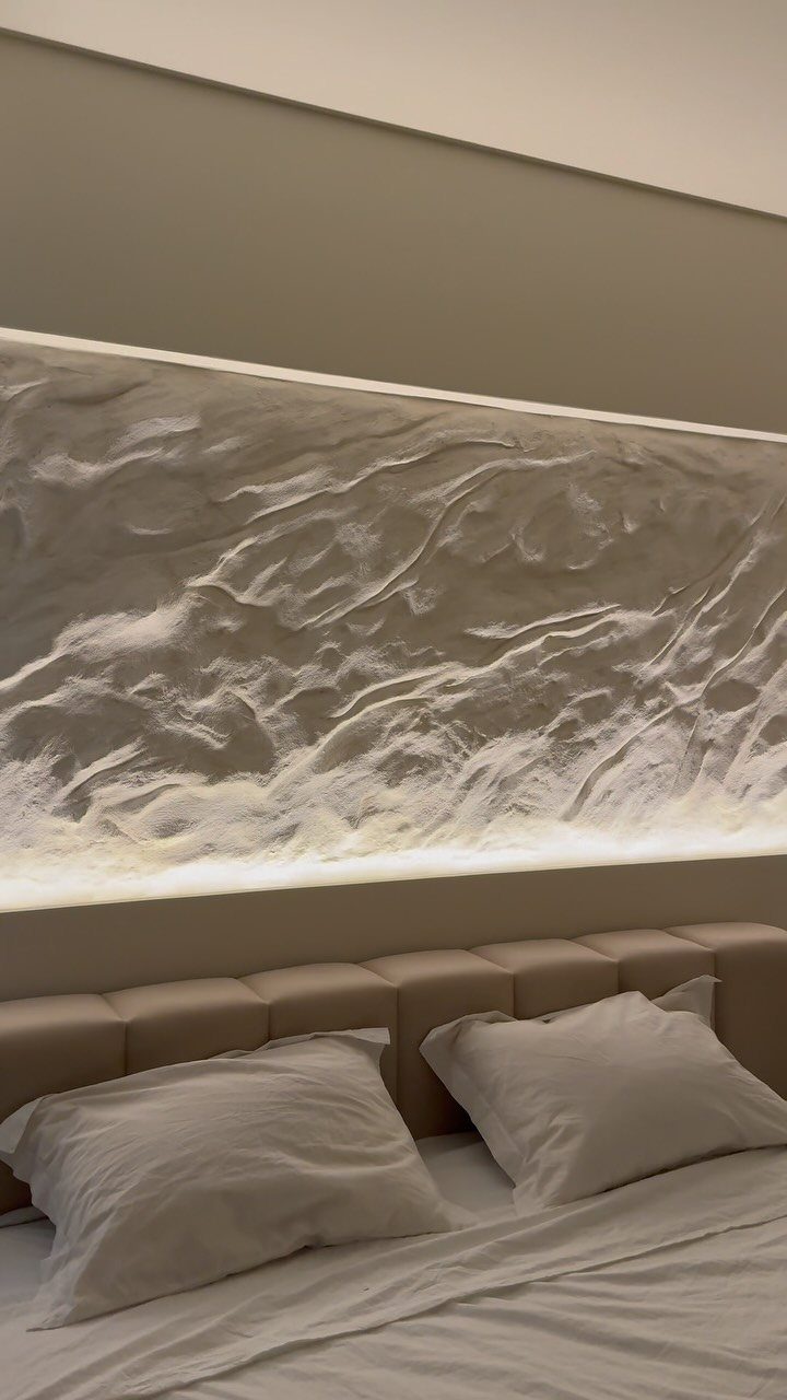Textured 3D wave feature wall with integrated lighting above a beige tufted headboard.