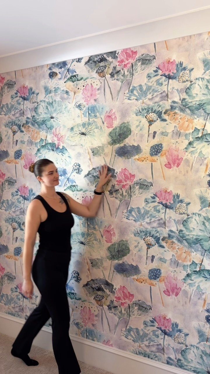 Woman standing next to a feature wall with pink lotus floral wallpaper.