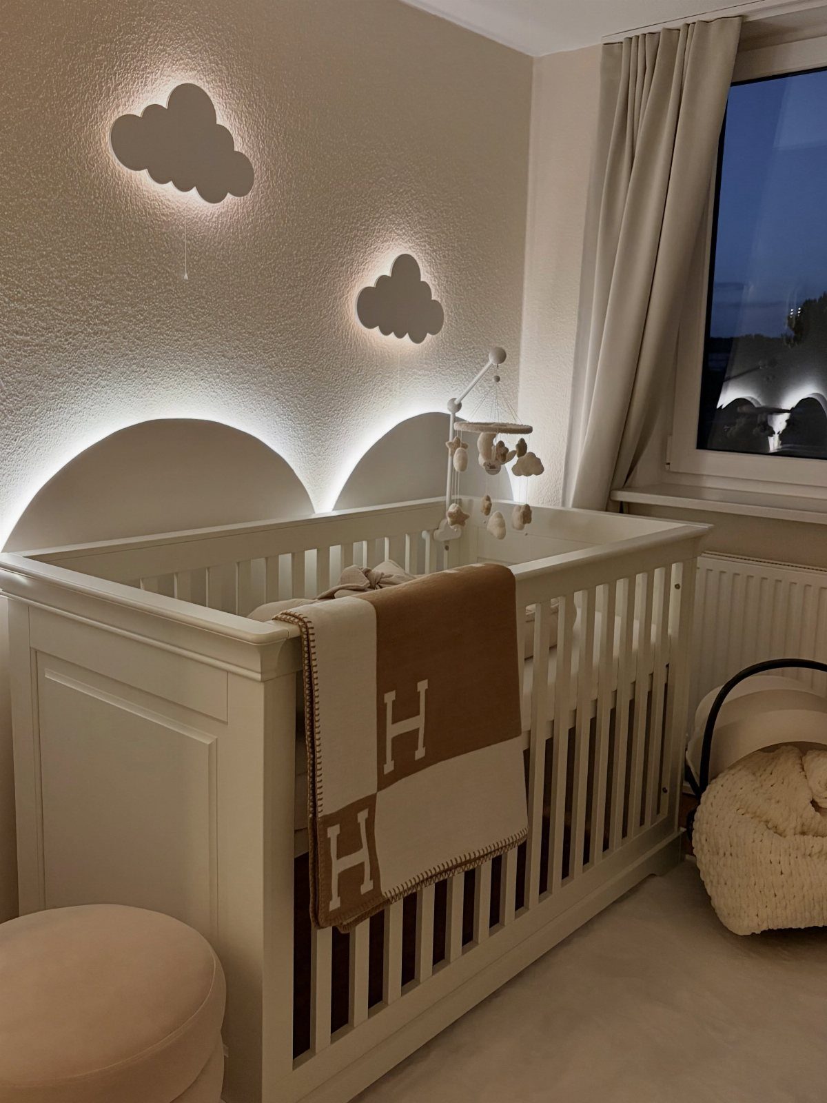 White baby crib with glowing cloud wall lights in a neutral nursery