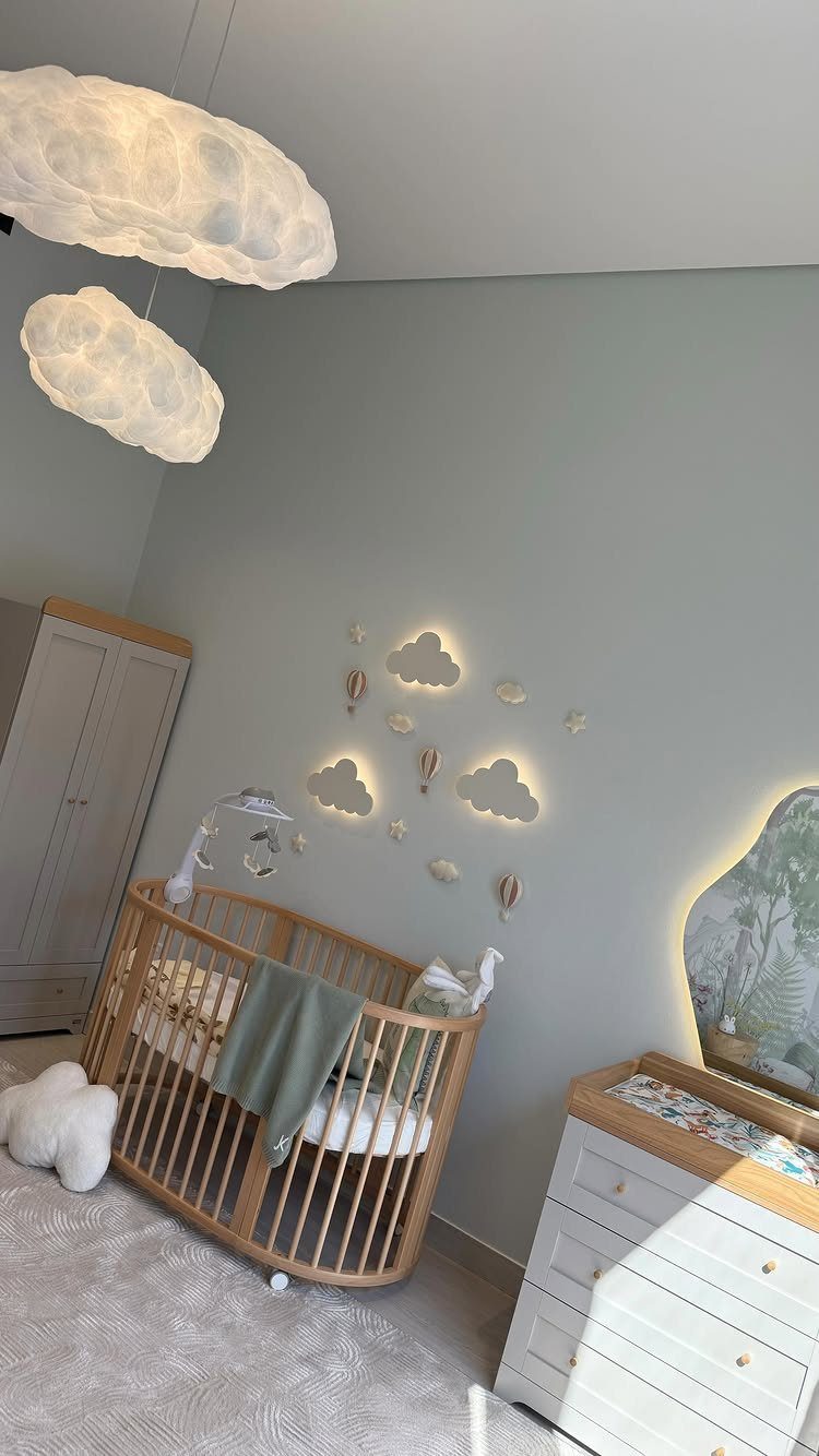 Wooden oval crib in a nursery with cloud lights and green walls
