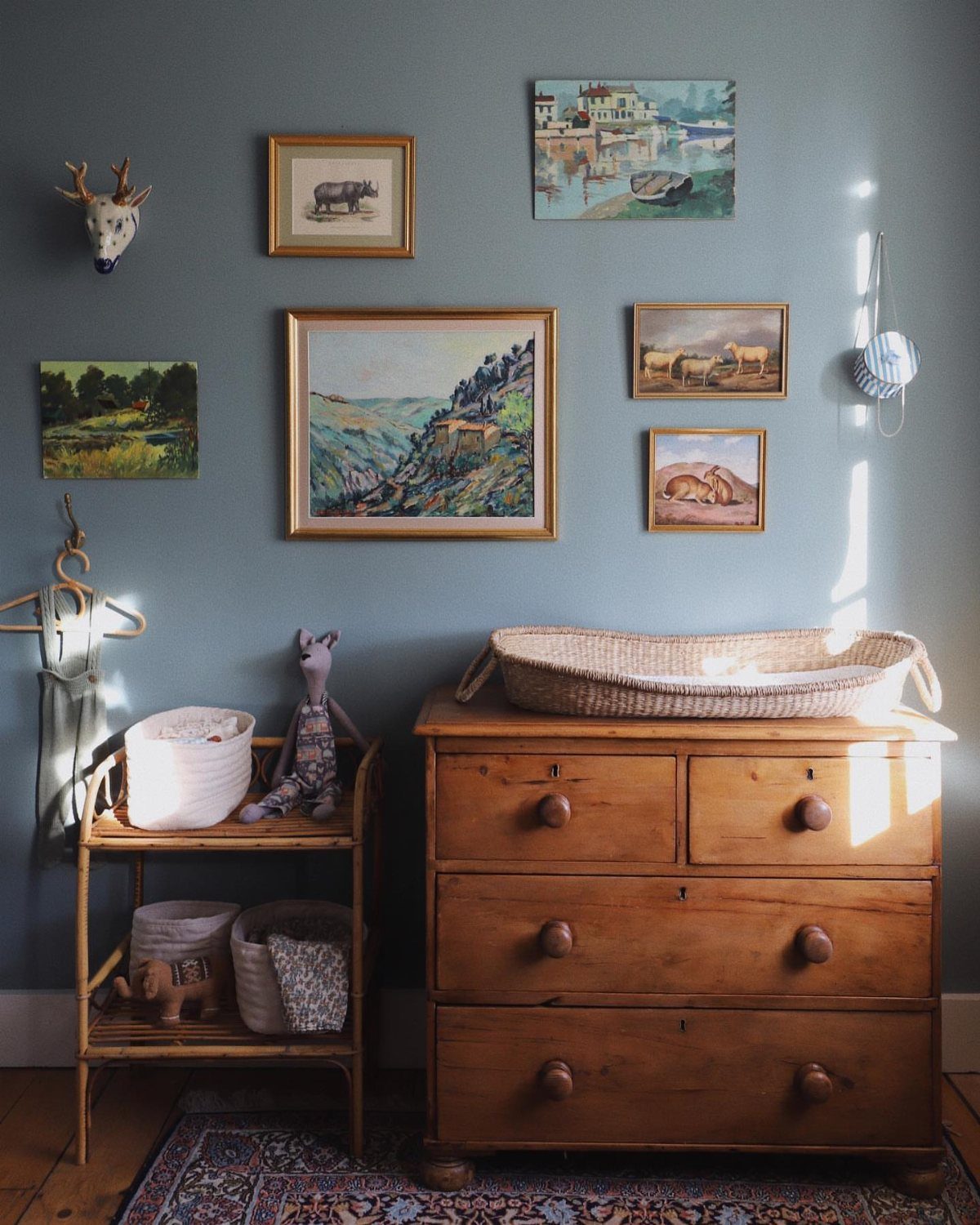 Wooden dresser and shelving unit in a nursery with nature-themed wall art.