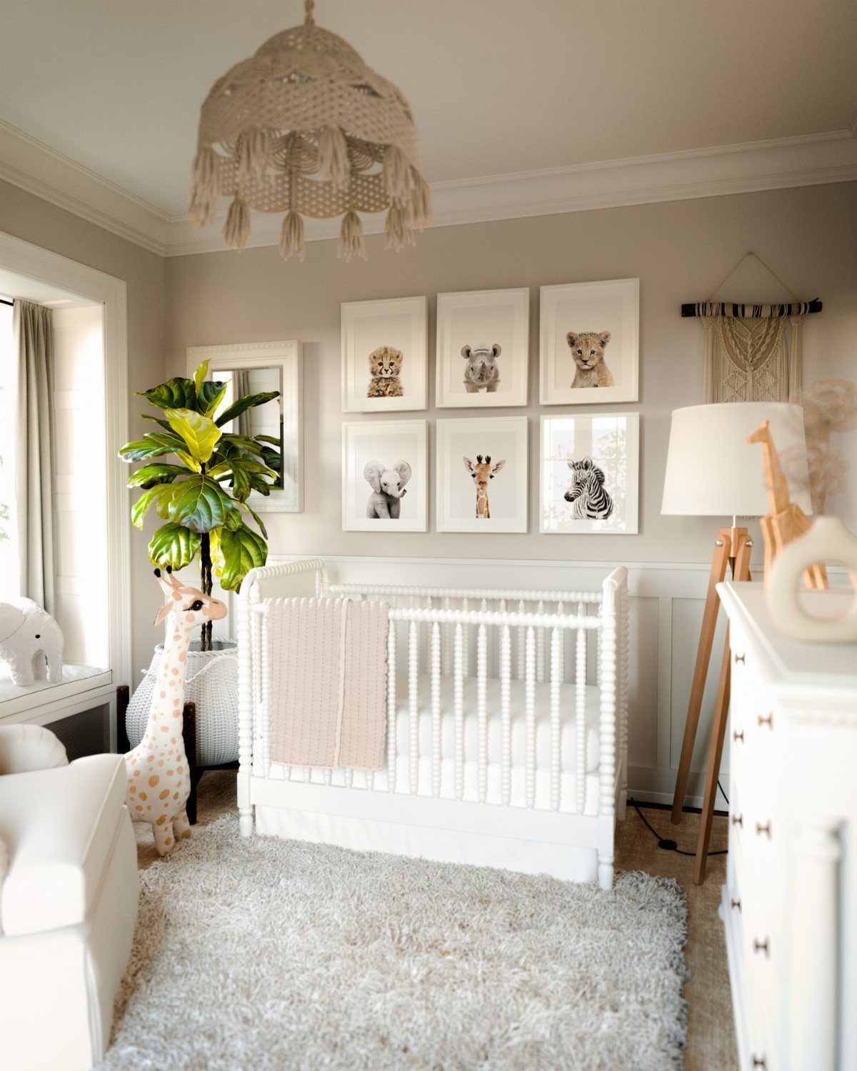 Neutral nursery with white crib, animal wall art, and a plush giraffe toy.