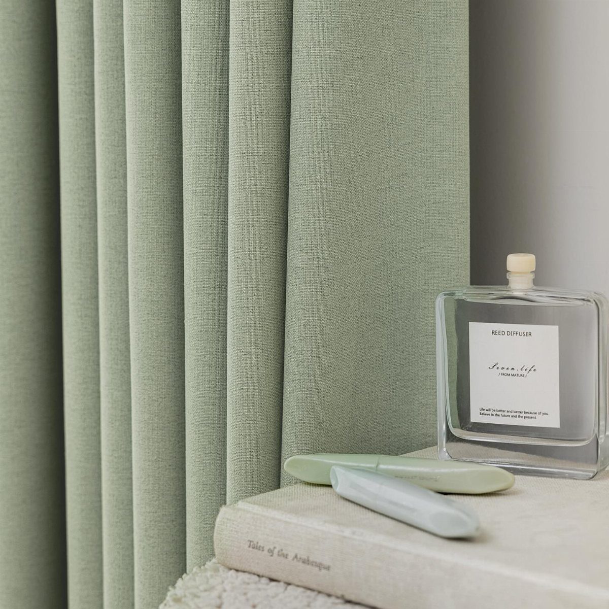 Sage green fabric curtains hanging next to a white wall with decorative accessories.