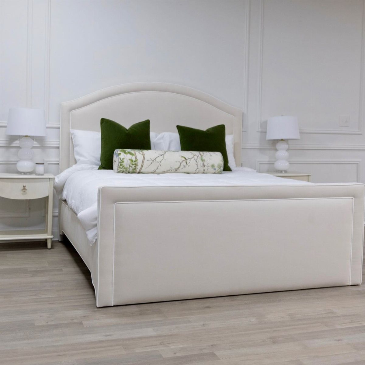White upholstered bed with curved headboard, green pillows, and white nightstands in bedroom