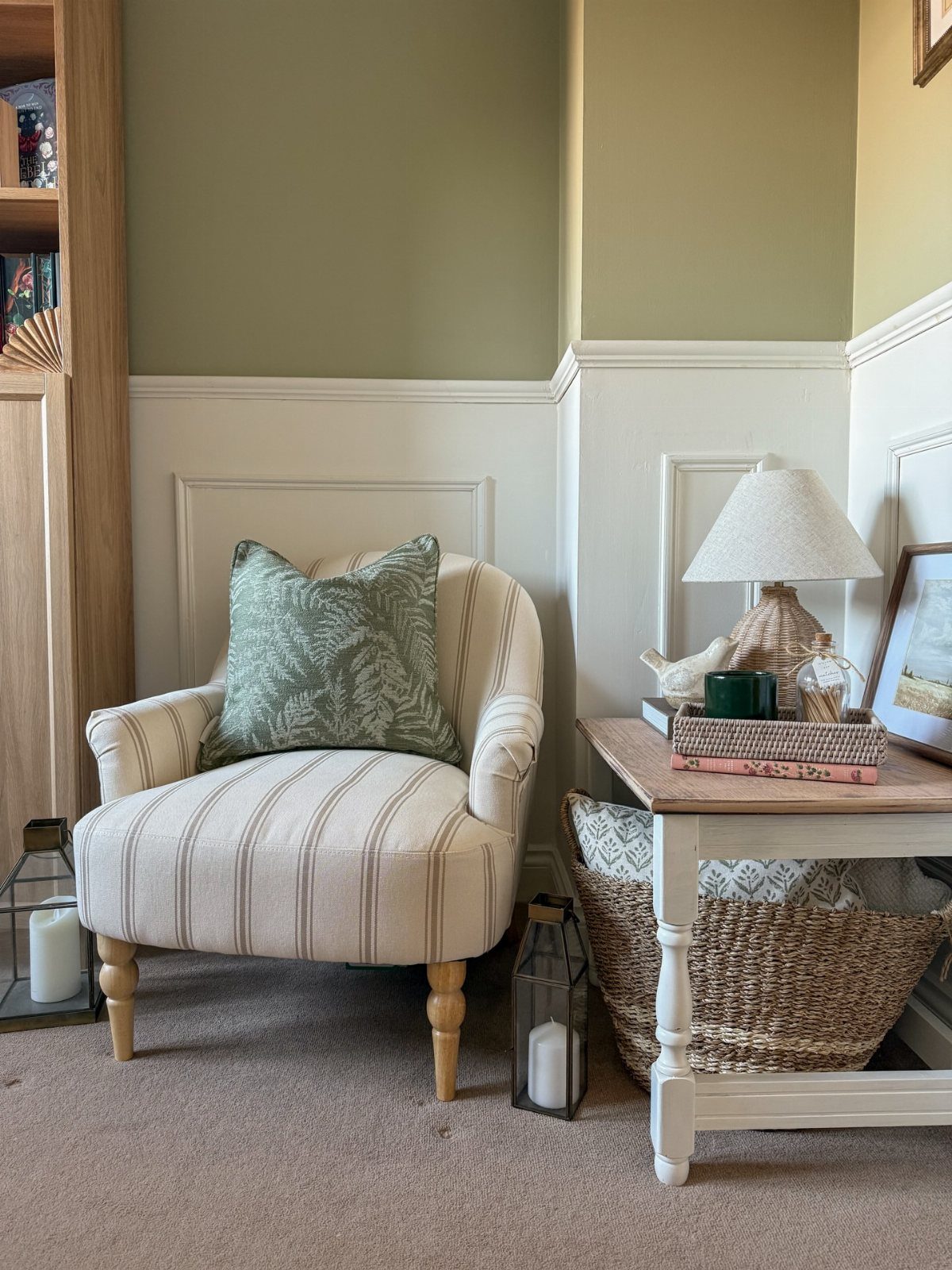 Striped armchair with sage green pillow in a reading nook with green walls.