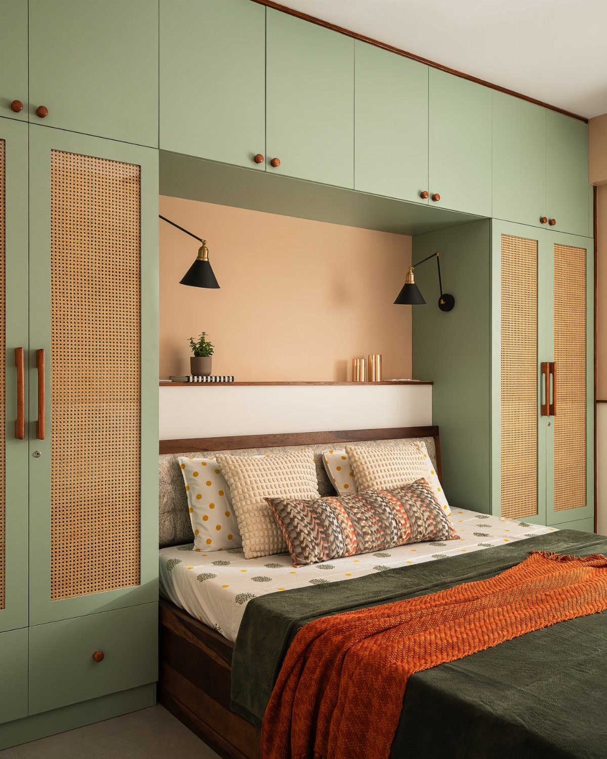 Sage green wardrobes with rattan inserts surrounding a bed with colorful linens.