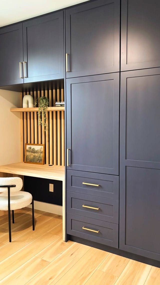 Home office nook with dark blue cabinets, light wood desk, and white chair.
