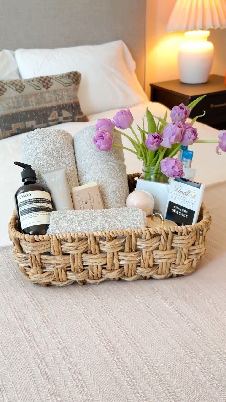 Woven basket with towels, toiletries, and purple tulips on a guest bed.