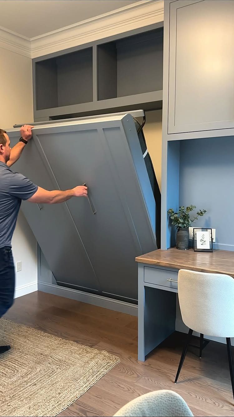 Man pulling down a grey Murphy bed next to a built-in wooden desk