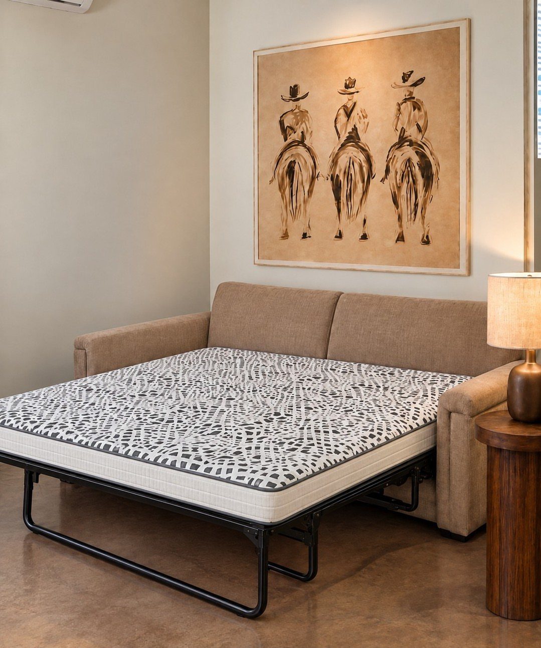 Tan sleeper sofa converted into a bed with a patterned mattress in a room.