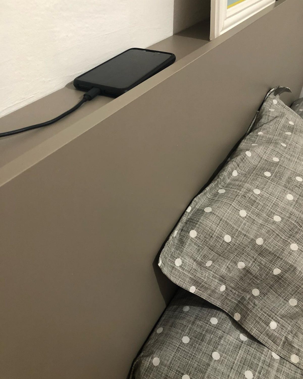 Grey flat-top headboard with a charging smartphone and polka-dot pillows.
