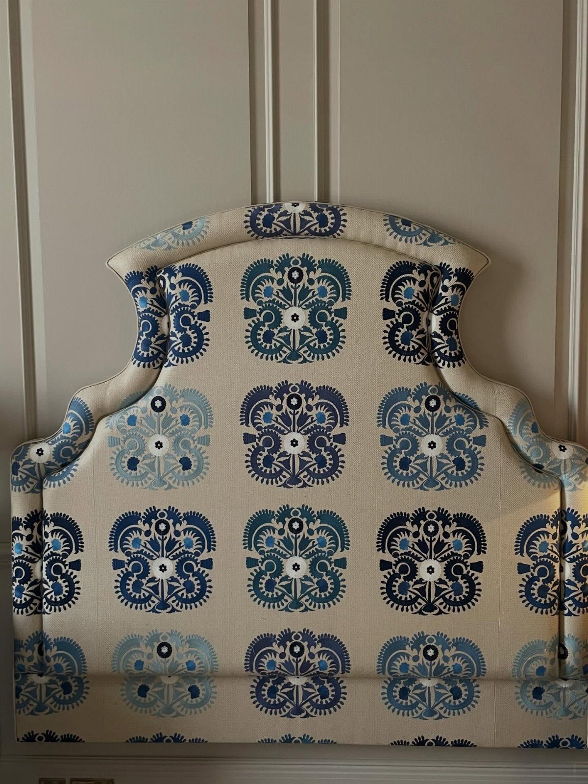 Upholstered headboard with blue floral patterns leaning against a grey paneled wall.