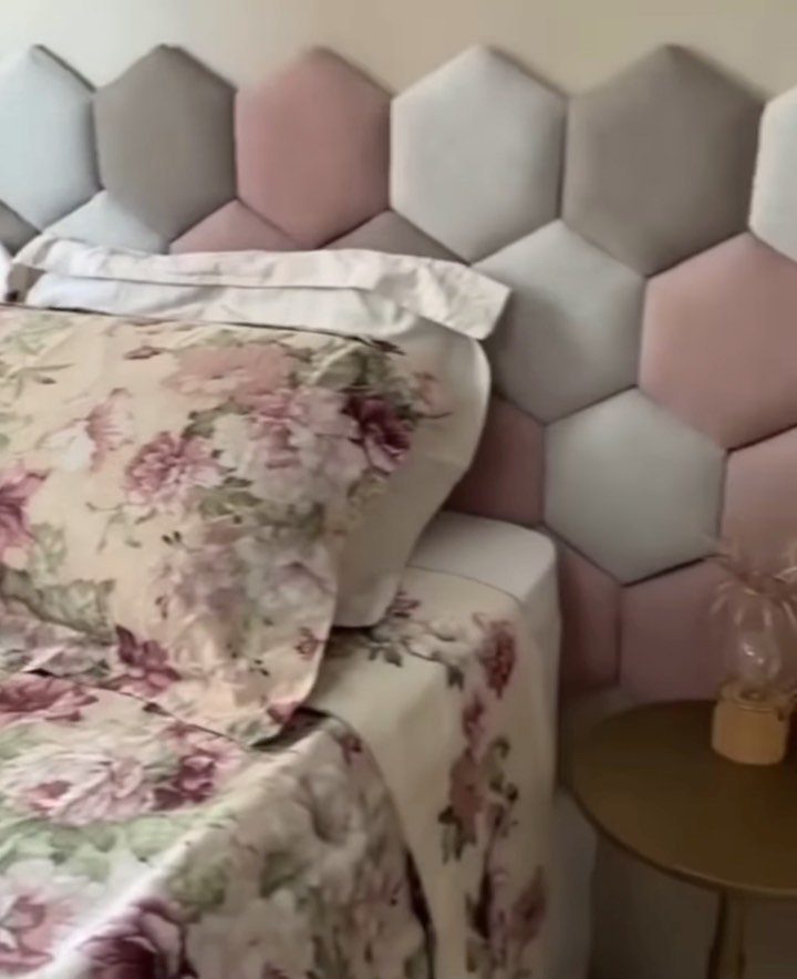 Hexagonal upholstered headboard in pink and grey behind a bed with floral sheets.