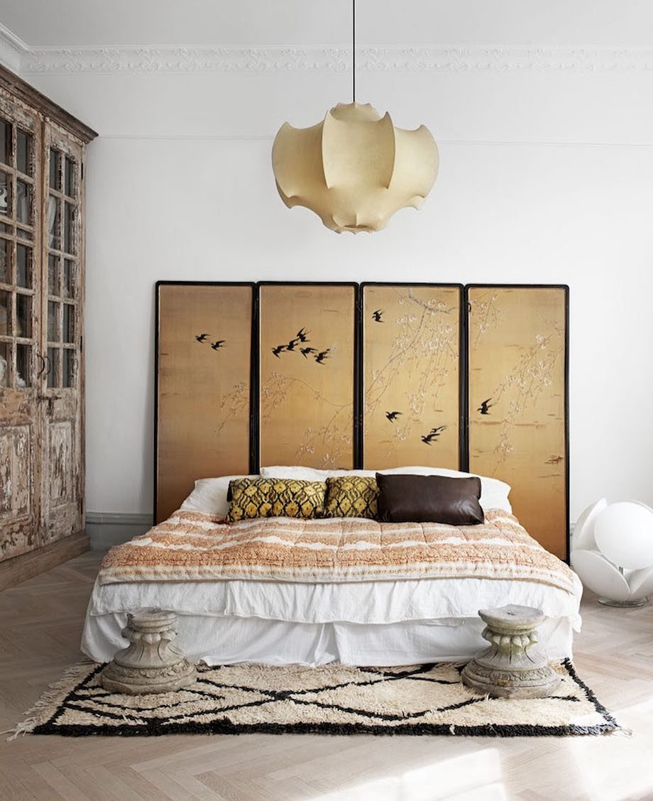 Gold folding screen with bird illustrations used as a headboard behind a bed.