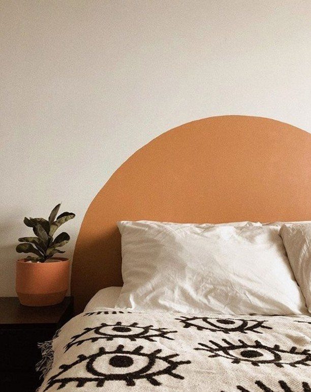 Terracotta semi-circle painted on a white wall as a headboard behind a bed.