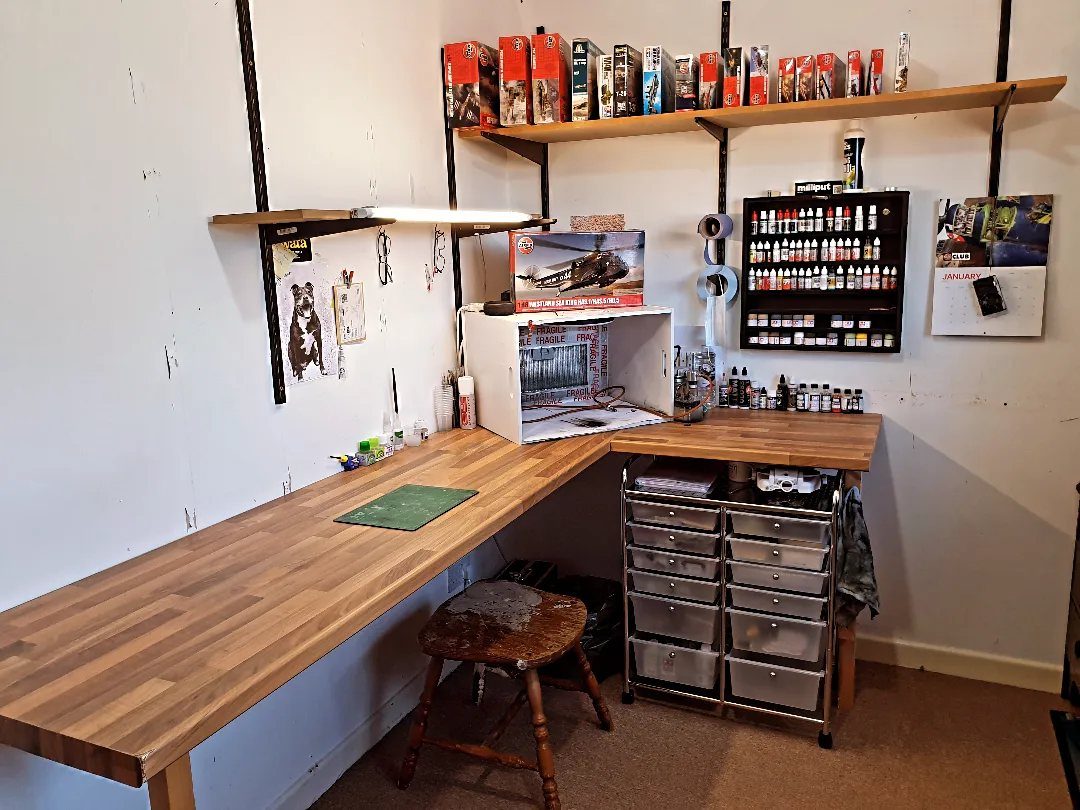 Wooden workbench with model kits and paint bottles in a dedicated hobby room.