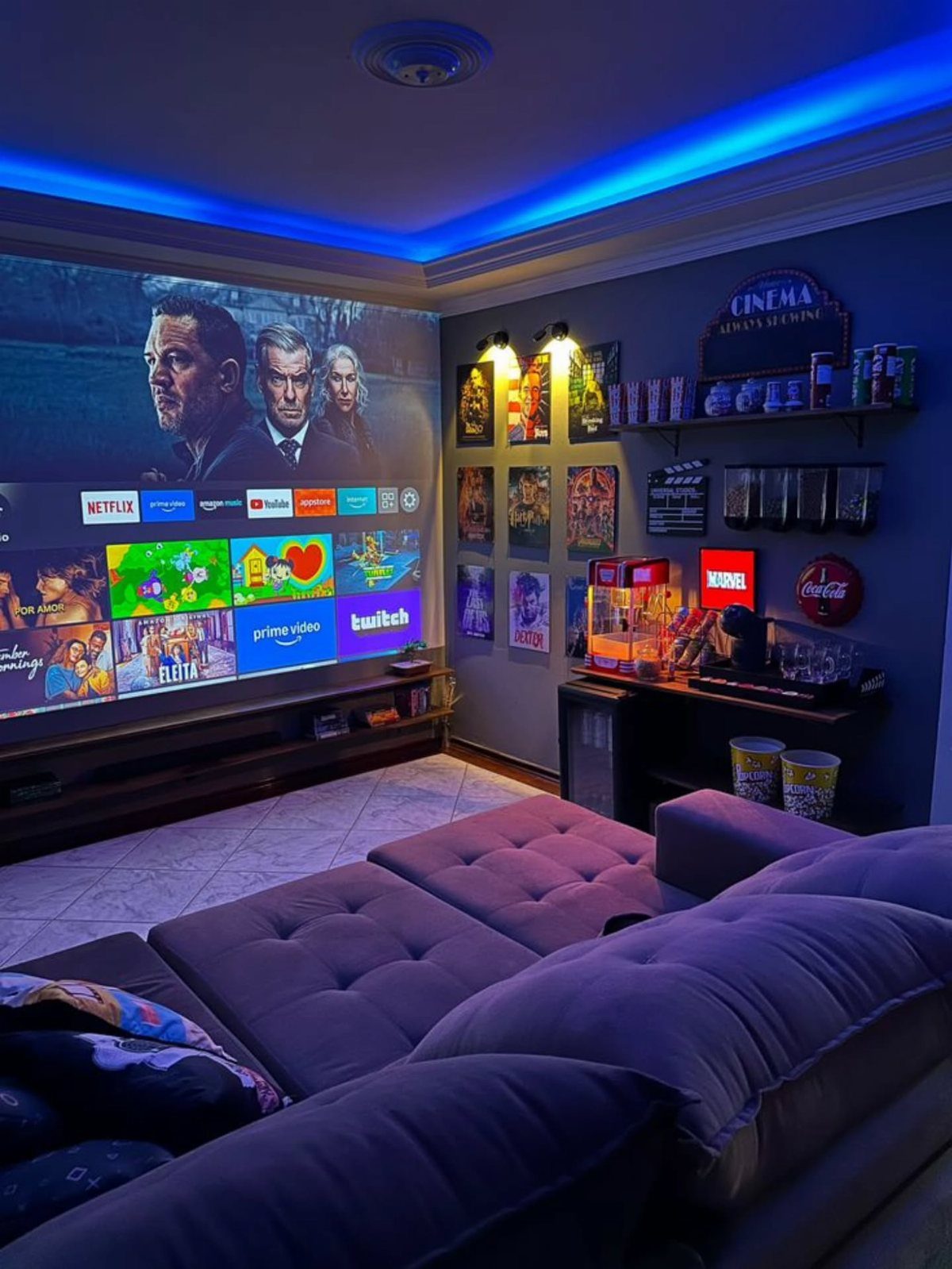 Home cinema room with large projector screen, purple modular sofa, and blue lighting.