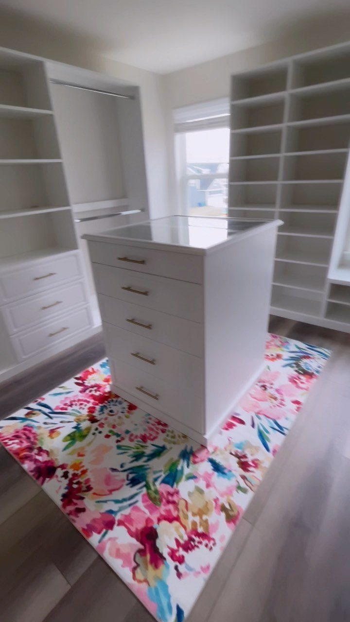 White walk-in closet with built-in shelving and a colorful floral area rug.