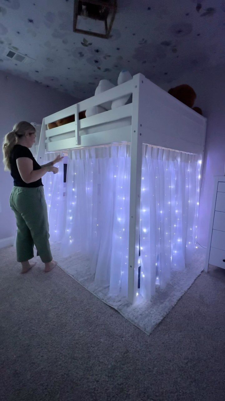 White loft bed with a cozy curtained area and fairy lights underneath.
