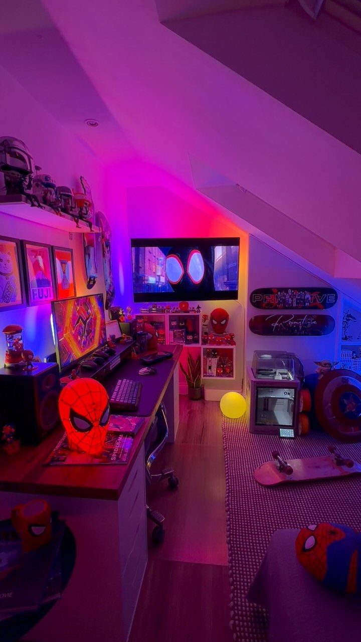 Gaming setup with neon purple lighting, monitors, and Spider-Man themed decor in a bedroom.