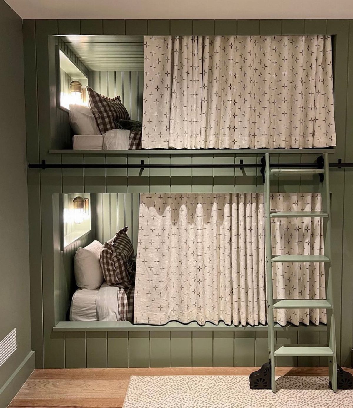 Built-in green bunk beds with white patterned curtains and a matching wooden ladder.