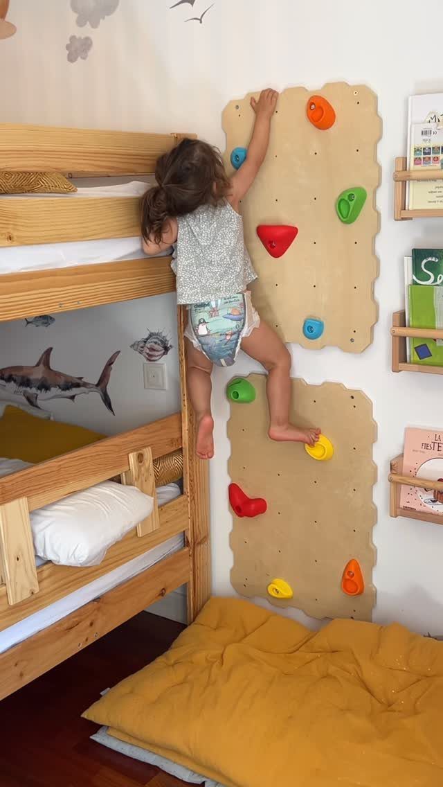 Child climbing a colorful rock wall installed next to a wooden bunk bed.