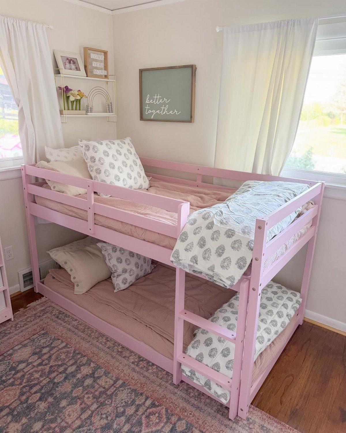 Pink wooden bunk bed with patterned bedding in a bright child's bedroom